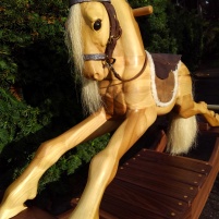 wooden rocking horse, with sun shining on it making the poplar wood glow with warm sand color.