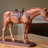 hand carved cherry wood horse standing with carved walnut saddle on walnut base. With carved bridle and rein over neck
