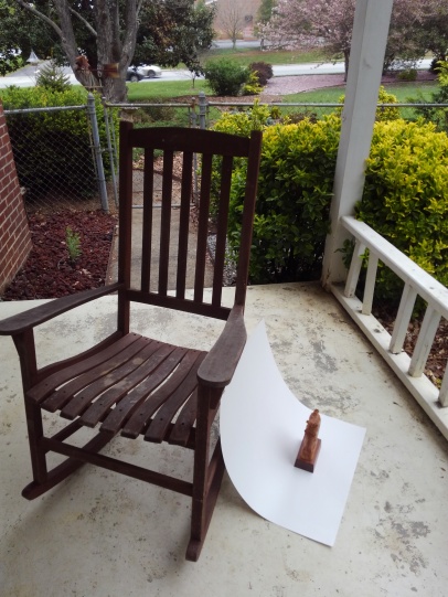 example of how to photograph small wood carving with a piece of white poster board taped to a rocking chair on an outdoor porch. Hand carved horse head sculpture is the subject being photographed